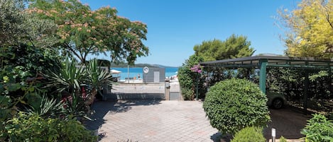 A paved pathway leading to a beachside area with a pergola and a car parked nearby.