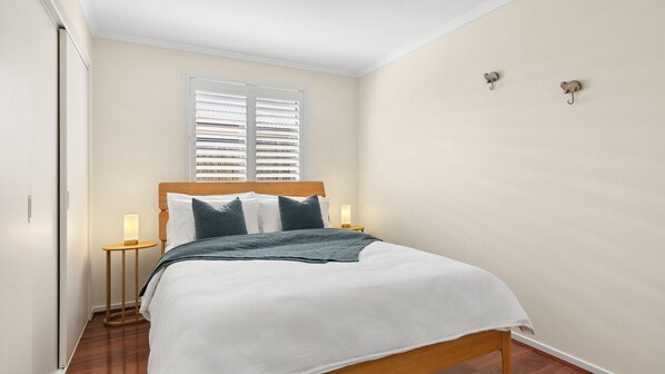A bedroom with a wooden bed, white bedding, two bedside lamps, and a window with blinds.