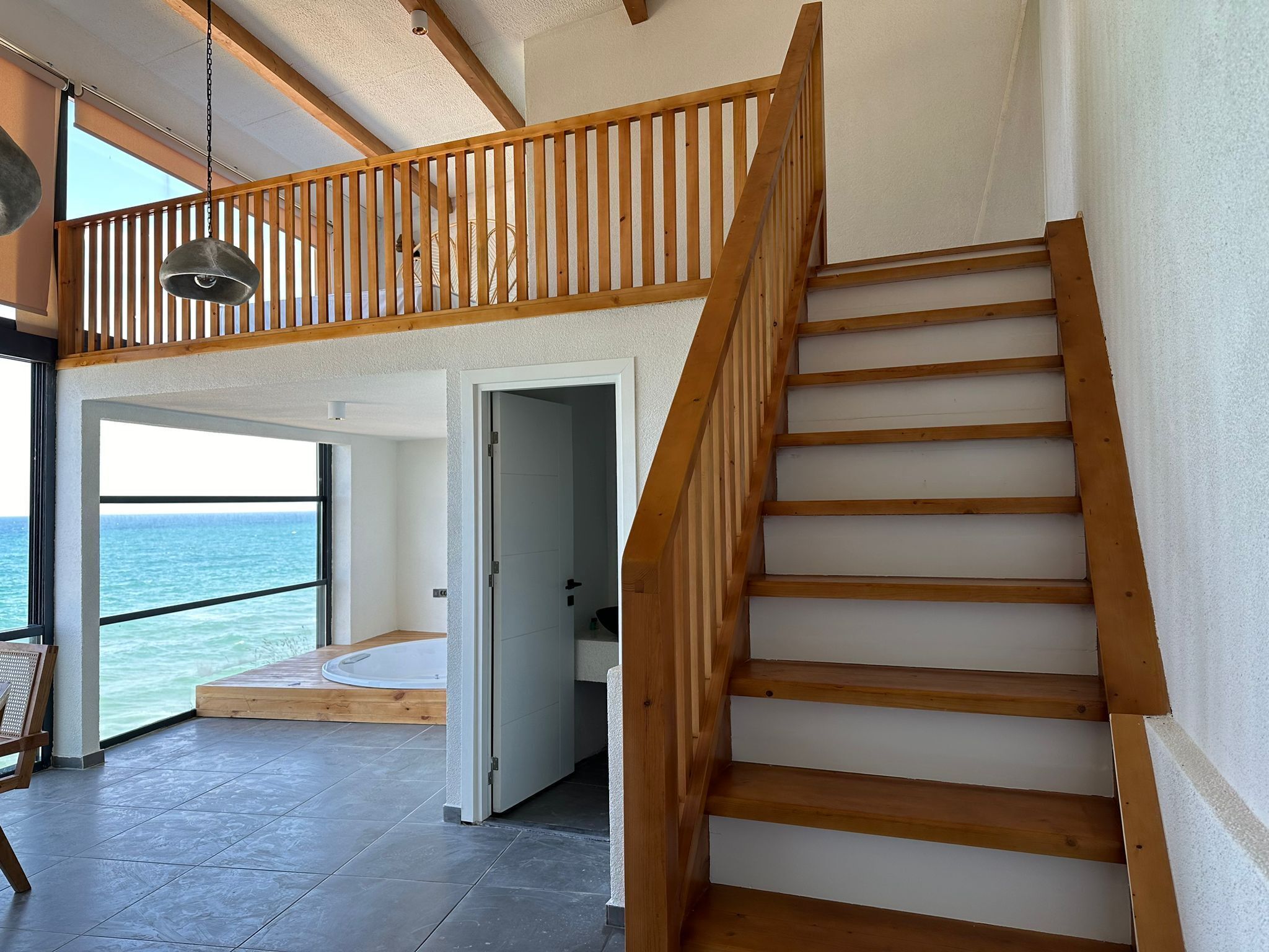 Amplia habitación con una escalera de madera, vista al mar y un ventanal grande.