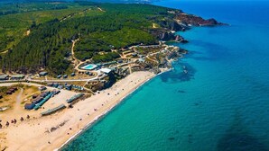 An aerial view of a coastal area with a beach, a forested hill, and a clear blue sea. - Sahil Kamp Istanbul Hotel (Sile)