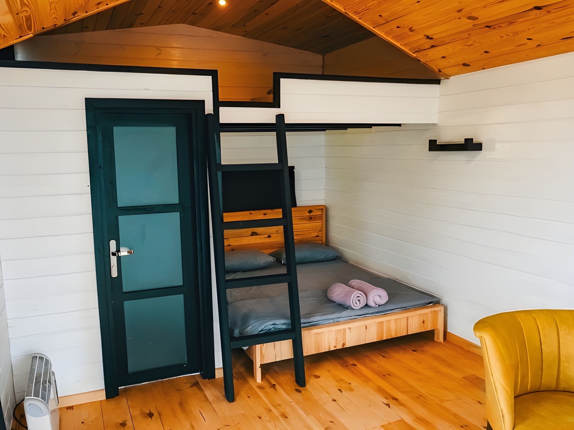 Une petite pièce avec un lit superposé, une chaise en bois et une porte dotée d’une poignée.