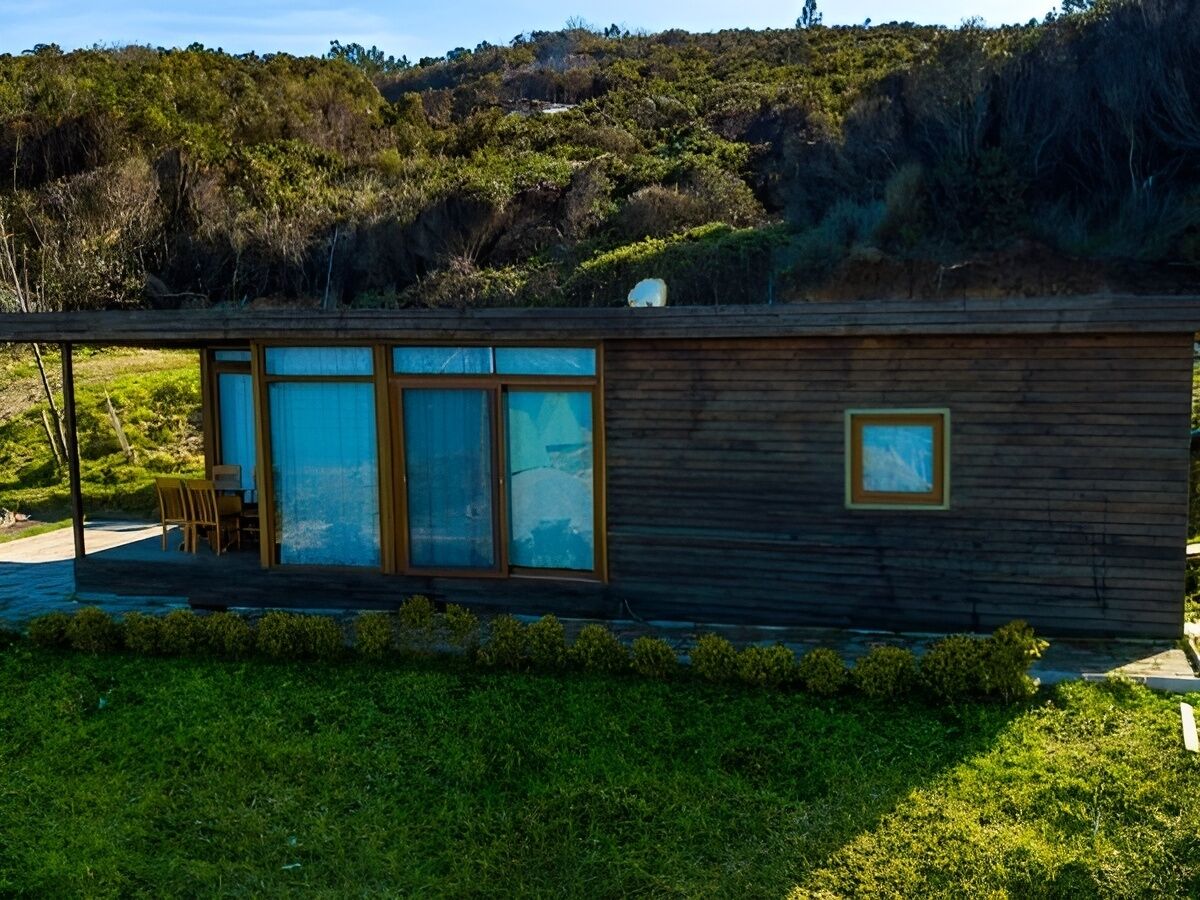 Una cabana de fusta moderna amb grans finestres, un petit balcó i una antena parabòlica.