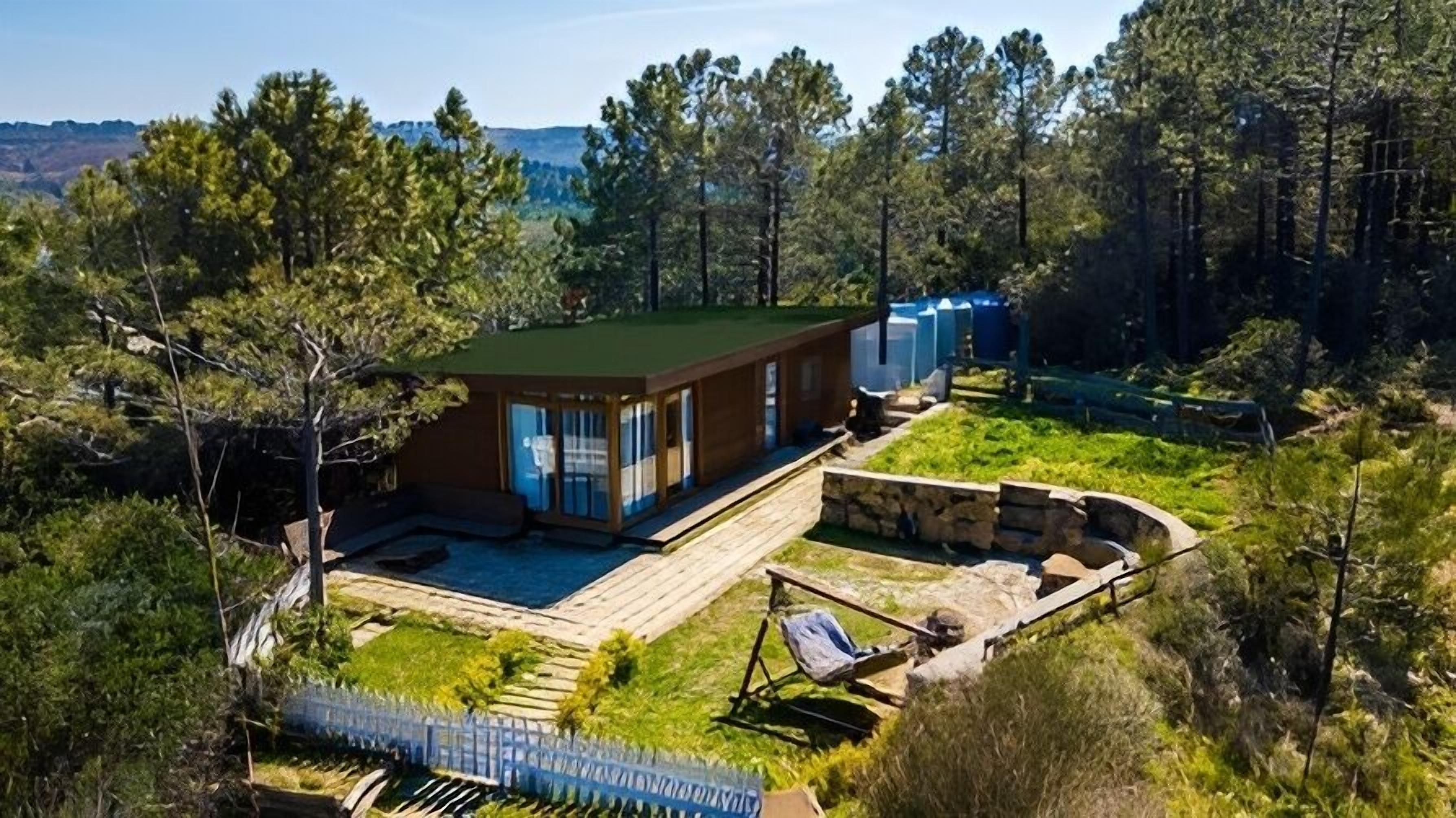 A modern cabin with a large deck, a swimming pool, and a stone fire pit.