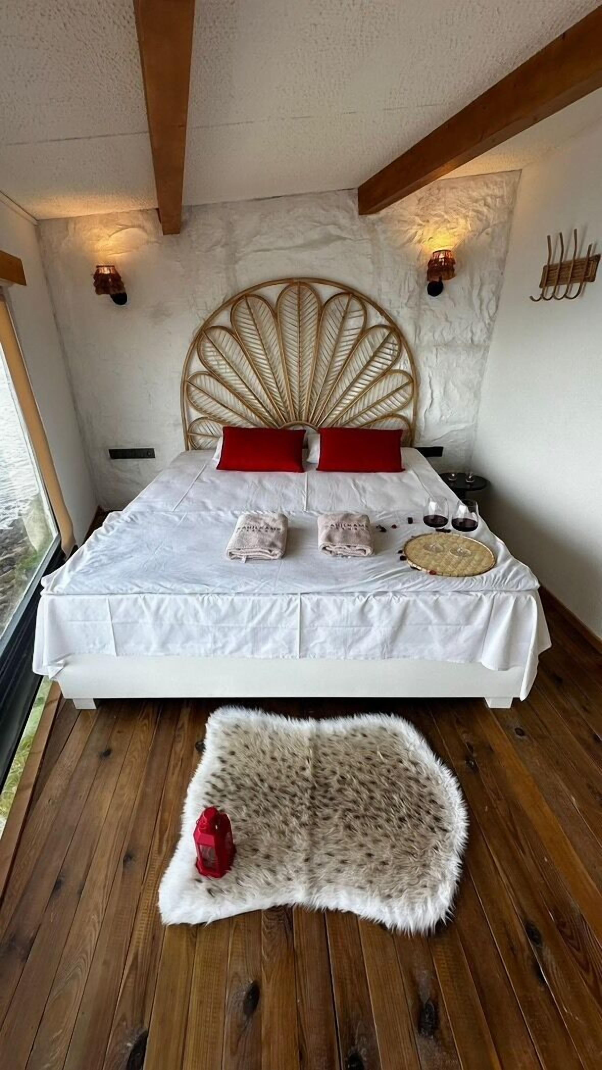 Un dormitorio con una cama grande, almohadas rojas, un cabecero y una alfombra pequeña.