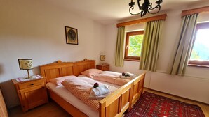 Un lit en bois avec une literie à carreaux, une table de chevet avec une lampe, une fenêtre avec des rideaux et un tapis à motifs.