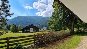 Un paysage rural avec une maison, une clôture en bois et une chaîne de montagnes en arrière-plan.