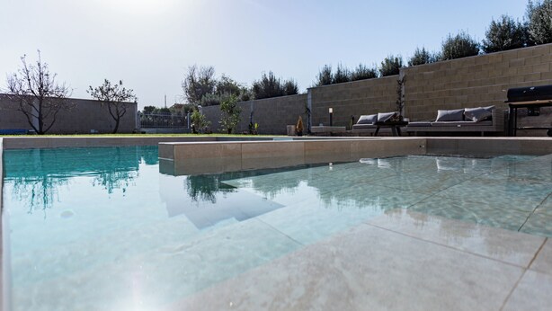 A swimming pool with clear water, surrounded by a stone wall and a few trees. - Villa with heated pool 2 steps from the sea (Quartu Sant'Elena)