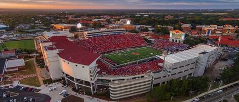 An aerial view of a stadium with a football field, surrounded by buildings and parking areas.