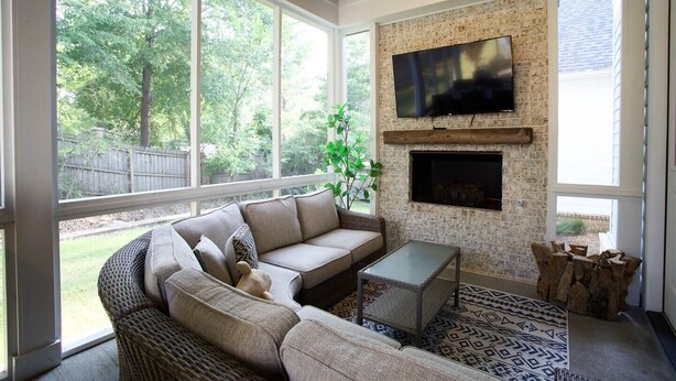 A sunroom with a stone fireplace, a large TV, wicker furniture, and a view of the backyard.