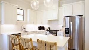 A modern kitchen with white cabinetry, a stainless steel refrigerator, a built-in oven, and a large island with chairs.