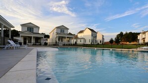 A swimming pool with adjacent houses, a covered patio, and a clear sky.