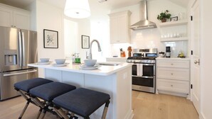 A modern kitchen with white cabinetry, stainless steel appliances, a central island with seating, and a large overhead light.