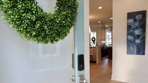 A modern interior with a green wreath on a door, a painting on the wall, and a kitchen area in the background.