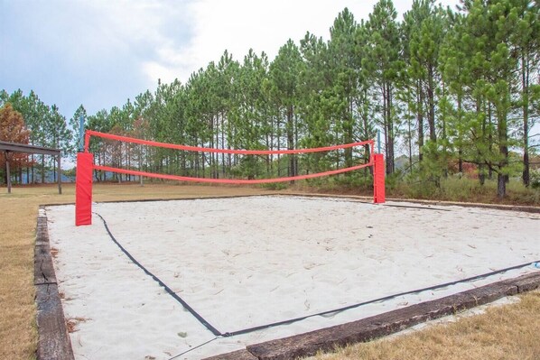 Una red de voleibol en una cancha de arena rodeada de árboles.