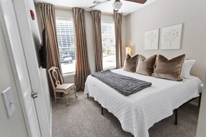 Ein Schlafzimmer mit Bett, Stuhl, einem Fenster mit Vorhängen und Wandbildern.