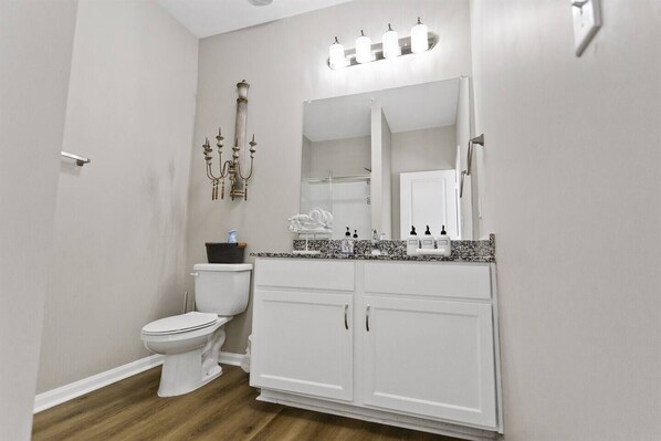 A bathroom with a toilet, a vanity with a mirror, and a light fixture above the mirror.