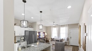 Una cocina moderna con encimeras de granito, electrodomésticos de acero inoxidable, iluminación colgante y un comedor con sofá y mesa de centro.