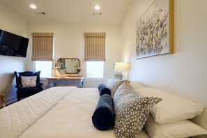 A hotel room with a bed, a desk with a chair, a television, and a painting on the wall. - The Bluebonnet - Stunning Southern Charm Retreat! (Oxford)