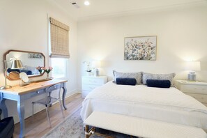 Un dormitorio con cama, mesitas de noche, escritorio, silla, espejo y un cuadro en la pared.