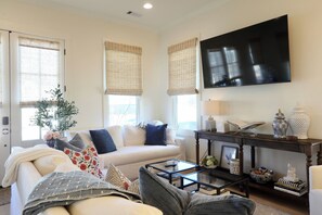 A living room with a sofa, coffee table, and a flat-screen TV mounted on the wall. - The Bluebonnet - Stunning Southern Charm Retreat! (Oxford)
