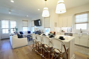 A modern kitchen with white cabinetry, a dining area with wicker chairs, and a living room with a white sofa. - The Bluebonnet - Stunning Southern Charm Retreat! (Oxford)
