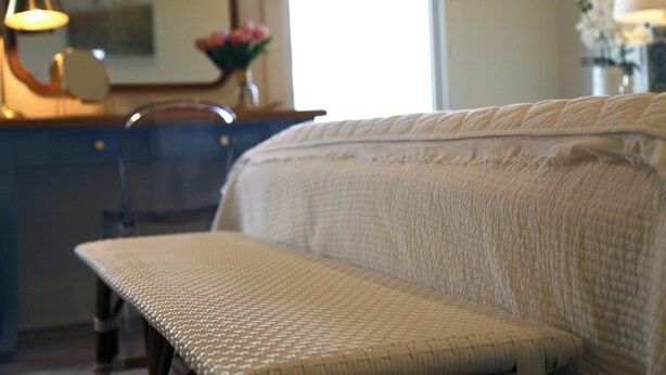 A room with a bed, a bench, a desk, and a lamp.