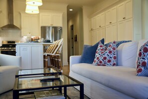 A modern living room with a white sofa, a glass coffee table, and a kitchen in the background. - The Bluebonnet - Stunning Southern Charm Retreat! (Oxford)