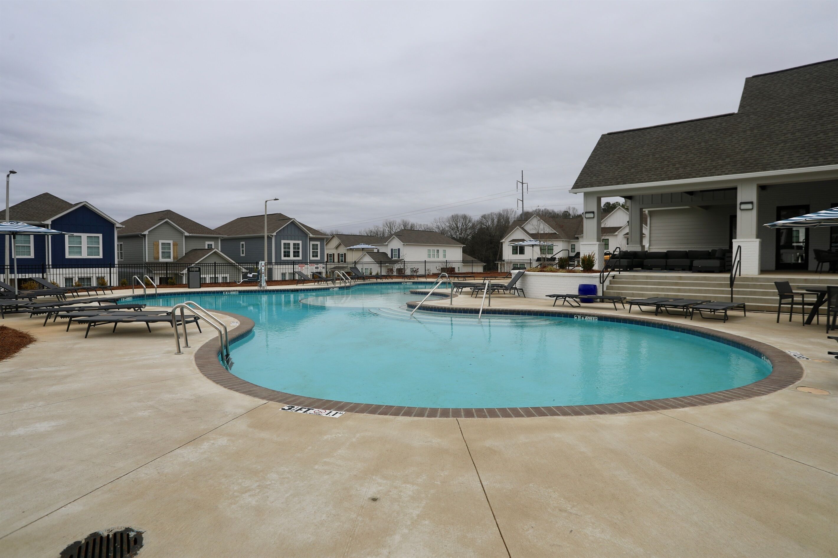 A swimming pool with lounge chairs and a covered area with tables and chairs.