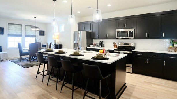 A modern kitchen with dark cabinets, a central island with bar stools, stainless steel appliances, and pendant lighting.