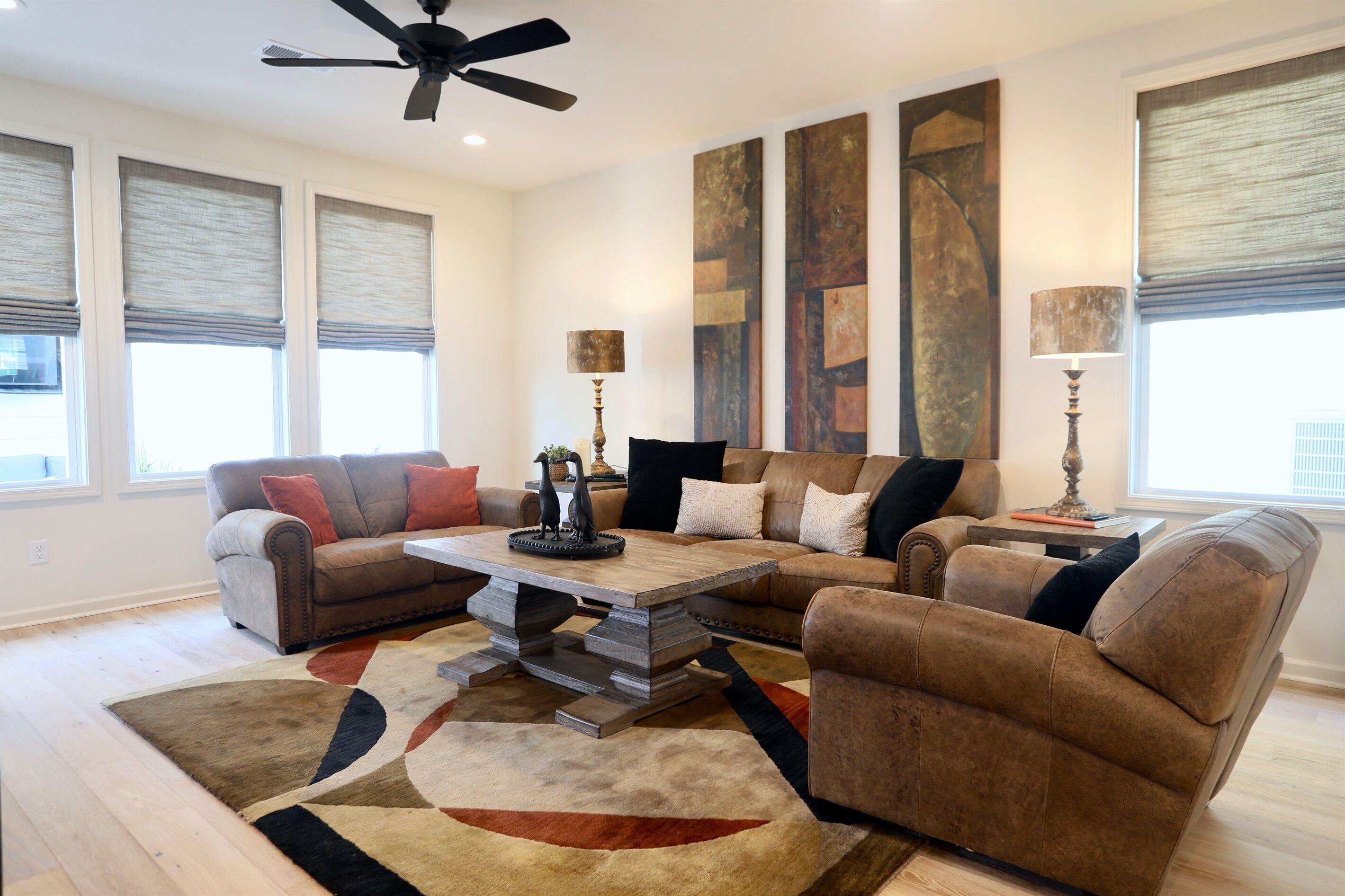 A living room with a sectional sofa, a coffee table, and a rug. There are two lamps on side tables, and artwork on the walls.
