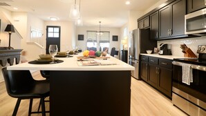 A modern kitchen with a central island, black cabinets, stainless steel appliances, and pendant lighting.