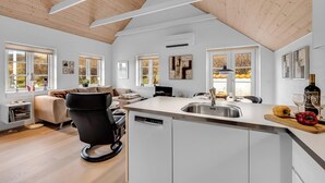 A modern kitchen with a central island, a dining area with a sofa, and a living room with a black chair. - Modernized holiday home, centrally located in one of Søndervig's best locations (Ringkøbing)