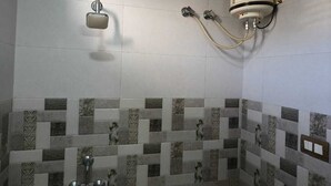 A bathroom with a tiled shower wall, a wall-mounted heater, and a hand shower. - Hotel Pangot Himalayan View (Kosiyakutoli)