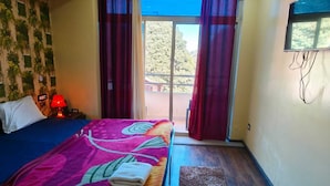 A room with a bed, a nightstand, a lamp, and a view of the outdoors through a glass door. - Hotel Pangot Himalayan View (Kosiyakutoli)