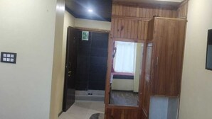 A hotel room with a wooden wardrobe, a television mounted on the wall, and a door with a green exit sign. - Hotel Pangot Himalayan View (Kosiyakutoli)