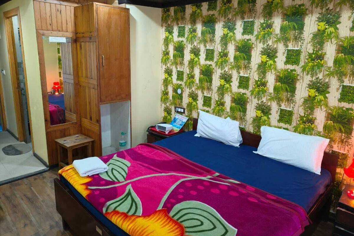 A bedroom with a bed, wooden wardrobe, and a wall with green plants.