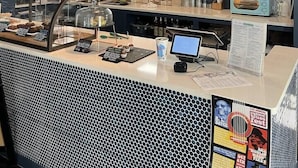 Interior de café com quadro de cardápio, balcão com vitrine e luminárias pendentes.
