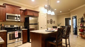 A kitchen with wooden cabinets, stainless steel appliances, a granite countertop, and a central island with bar stools. - The Great Southern - Chic Oxford Getaway (Oxford)