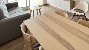 A modern living room with a wooden dining table, a grey sofa, and a white chair.