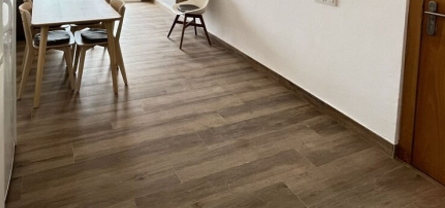 A hallway with a wooden floor, a dining table with chairs, and a white wall.