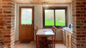 A dining area with a wooden table and chairs, a window with a view of greenery, and a brick wall. - Cottage in Sologne with enclosed garden, pets allowed, parking and internet (Neung-sur-Beuvron)