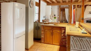 A kitchen with a white refrigerator, wooden cabinets, a brick wall, and a wooden ceiling. - Cottage in Sologne with enclosed garden, pets allowed, parking and internet (Neung-sur-Beuvron)