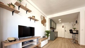 A modern living room with a flat-screen TV, wooden shelves, and a kitchen area in the background. - Apartment 10m to Beach, A/C, WiFi, Sleeps 4 (Salou)