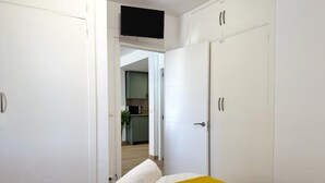 A bedroom with a bed, white wardrobes, a television mounted above the bed, and a view into a kitchen area. - Apartment 10m to Beach, A/C, WiFi, Sleeps 4 (Salou)