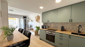A modern kitchen with a wooden dining table, two chairs, a microwave, a coffee maker, and a patterned backsplash. - Apartment 10m to Beach, A/C, WiFi, Sleeps 4 (Salou)