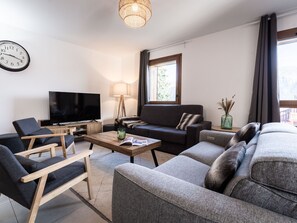 Ein modernes Wohnzimmer mit Flachbildfernseher, einer Couch, einem Couchtisch und einer Lampe.