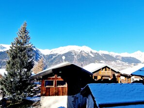 Eine Holzhütte mit geneigtem Dach, umgeben von schneebedeckten Bergen und blauem Himmel.