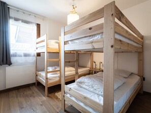 Habitación con literas, suelo de madera, ventana con cortinas y una lámpara colgante.