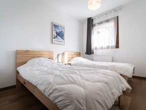 Ein Schlafzimmer mit einem hölzernen Bett, einem Nachttisch, einer Lampe, einem Fenster mit Vorhängen und einem gerahmten Bild an der Wand.