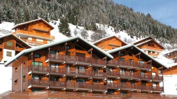 Un chalet à plusieurs étages, doté de balcons, qui se dresse sur fond de montagnes enneigées.